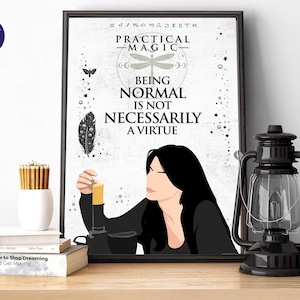 Pode incluir: Uma impressão emoldurada com as palavras "Practical Magic" e "Being Normal Is Not Necessarily A Virtue". Uma mulher é retratada segurando uma vela. Uma lanterna preta e um vaso branco com lápis estão em uma superfície de madeira.