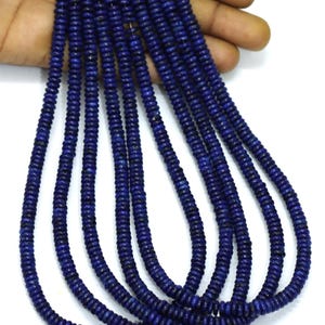 Puede incluir: Múltiples hilos de pequeñas cuentas en forma de disco de un color azul real profundo y saturado. Cada hilo está ensartado en un filamento fino y claro, mostrando un patrón uniforme y repetitivo de cuentas circulares con una superficie ligeramente texturizada.