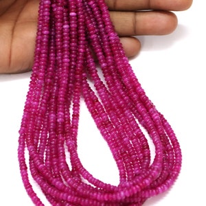 Op de afbeelding: Een streng roze edelsteen kralen. De kralen zijn klein en rond en zijn geregen op een dunne draad. De streng is lang en ligt over een hand.