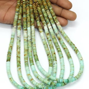 Peut inclure: Plusieurs brins de perles de pierres précieuses dans des tons de vert et de blanc. Les perles sont petites, plates et rondes, avec une texture légèrement irrégulière. La couleur passe d'un vert plus foncé à une teinte plus claire, presque turquoise. Les perles sont enfilées, prêtes pour la création de bijoux.