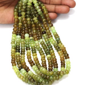 Pode incluir: Um fio de contas de pedras preciosas verdes e marrons. As contas são redondas e têm um acabamento liso e polido.