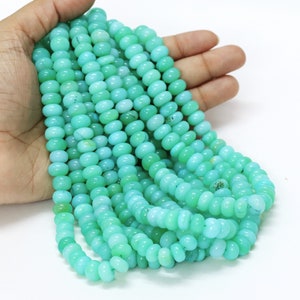 Puede incluir: Cadenas de cuentas de piedras preciosas de color azul verdoso claro. Las cuentas son de forma ovalada y tienen una superficie lisa y pulida. Las cuentas están ensartadas, formando múltiples cadenas. El color es una mezcla de azul claro y verde.