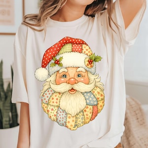 May include: Cream-colored t-shirt featuring a colorful Santa Claus graphic. Santa's face is detailed with a long white beard and a red and white polka-dotted hat. The graphic has a patchwork design with floral and geometric patterns.