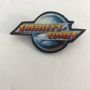 Puede incluir: Una colorida pegatina con el logotipo de Frehley's Comet. El diseño presenta el texto "FREHLEY'S COMET" en naranja y amarillo, con un gráfico de planeta azul y blanco. La pegatina tiene un borde negro y el texto "©1987 Paul Frehley".