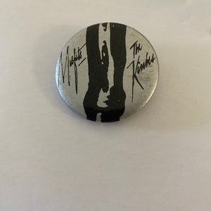 Peut inclure: Un bouton argenté avec une image en noir et blanc de jambes et le texte "Midnight" et "The Kinks" en noir.