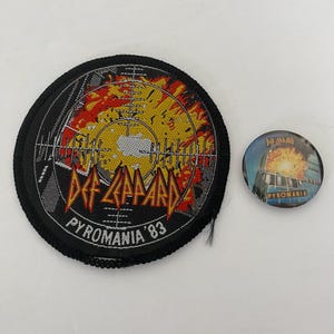 May include: A Def Leppard "Pyromania '83" patch and button. The patch is round, black, and features the band's logo in red and yellow, with a target design and the text "Pyromania '83". The button has the same design.