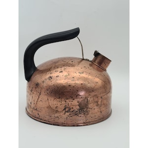 May include: A copper-colored kettle with a black handle and spout. The kettle has a rounded body and a curved handle. The kettle has the words "Paul Revere" printed on the side. The kettle is likely used for boiling water.