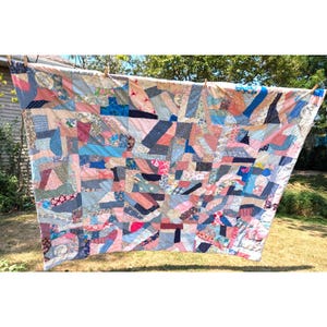 May include: A rectangular patchwork quilt featuring a chaotic arrangement of fabric scraps in various shades of blue, pink, white, and patterned textiles. The quilt is constructed from numerous irregular geometric shapes stitched together.