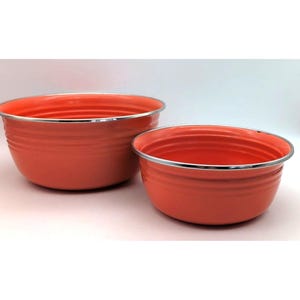 May include: Two round, coral-colored mixing bowls with a smooth, glossy finish and horizontal ribbed detailing along the exterior. Each bowl features a thin, polished silver-toned metal rim around the top edge, providing a clean, metallic contrast.