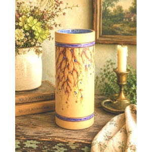 May include: A cylindrical ceramic vase with a matte beige finish, featuring a hand-painted design of cascading golden-brown leaves and small blue accents. The vase has thin blue horizontal bands at the top and bottom rims and a blue interior.