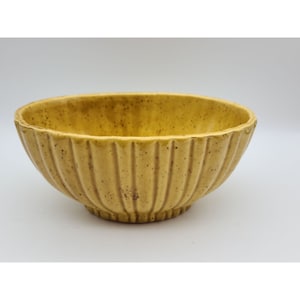 May include: A yellow ceramic bowl with a ribbed design. The bowl has a speckled finish and is perfect for serving snacks or holding small items.
