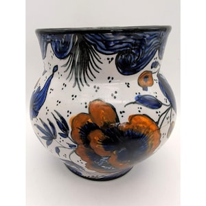May include: A hand-painted ceramic vase with a wide, rounded body and a slightly flared rim. The vase features a white base adorned with orange and blue floral designs, accented with black and blue details. The rim is painted black.