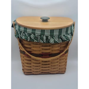 May include: A woven wicker basket with a wooden lid and a green and white striped fabric lining. The basket has a brown leather handle and a dark green knob on the lid.