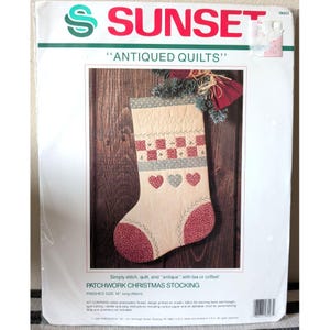 Peut inclure: Un kit de loisirs créatifs Sunset pour une chaussette de Noël en patchwork vieilli. L'emballage présente une chaussette beige avec des accents en tissu à motifs rouges et gris, des motifs de cœurs et le prénom Christopher brodé.
