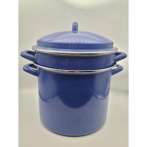 May include: A blue enamelware cooking pot with a lid and a steamer insert. The pot has two handles on each side and a silver rim. The lid has a small handle on top. The pot is a dark blue color with white speckles.