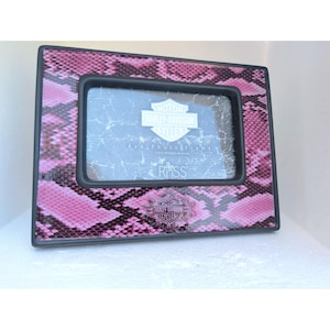 May include: A rectangular photo frame with a pink and black snakeskin pattern. The frame features a black border and a central insert displaying the Harley-Davidson logo, the text 4 x 6 Photo Frame, and the Russ brand name in white lettering.