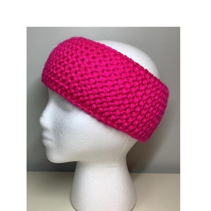 May include: A vibrant, hot pink crocheted headband. The thick, textured band is displayed on a white foam head. The headband is a solid color and appears to be made of a soft yarn. This accessory is perfect for keeping hair out of the face.