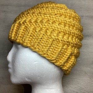 Puede incluir: Un gorro de punto amarillo con un patrón de punto texturizado.