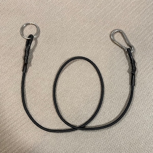 May include: A black bungee cord with a silver ring on one end and a silver carabiner on the other end.