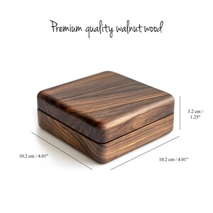 Może przedstawiać: Kwadratowe drewniane pudełko wykonane z drewna orzechowego. Pudełko ma wymiary 10,2 cm x 10,2 cm x 3,2 cm.