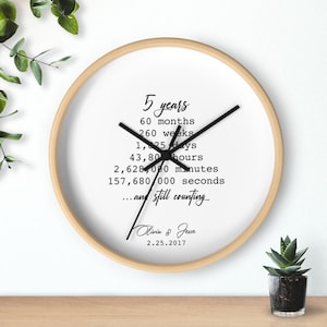 May include: A white clock with a wooden frame displays the time in years, months, weeks, days, hours, minutes, and seconds. The clock also includes the text "...and still counting" and the names "Olivia & Jesse" with the date "2.25.2017".
