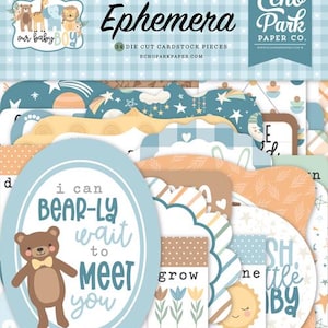 Könnte beinhalten: Eine Sammlung von gestanzten Kartonstücken mit Baby-Motiven. Die Teile zeigen einen Teddybären, eine Sonne, einen Mond und verschiedene Formen mit Sätzen wie „Ich kann es kaum erwarten, dich kennenzulernen“. Farben: Blau, Beige und Gelb.