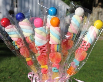 May include: A clear glass vase filled with colorful round gumballs, containing several candy skewers wrapped in clear plastic. Each skewer features a stack of multi-colored marshmallows, gummy ribbons, and a round candy topper in various bright hues.