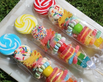 May include: Three colorful lollipop skewers with a variety of candies, including gummy bears, sour candies, and sprinkles. The lollipops are blue, yellow, and red.