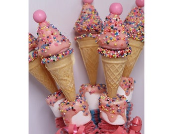 May include: A bouquet of edible treats featuring miniature waffle cones filled with pink icing and topped with a pink candy sphere. Each cone is decorated with multicolored sprinkles and sits atop a marshmallow base with pink glaze and sprinkles.