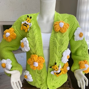 May include: A lime green knitted cardigan with a cable knit pattern and crocheted flower and bee embellishments.