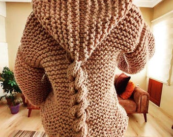 May include: A brown knitted cardigan with a large hood and a braided detail down the back.