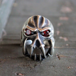 Op de afbeelding: Een zilveren schedelring met rode edelsteenogen en scherpe tanden.