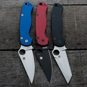 May include: Three pocket knives with different colored handles: blue, red, and black. The blades are all silver and have the Spyderco logo on them. The handles have the Spyderco logo and model name printed on them.
