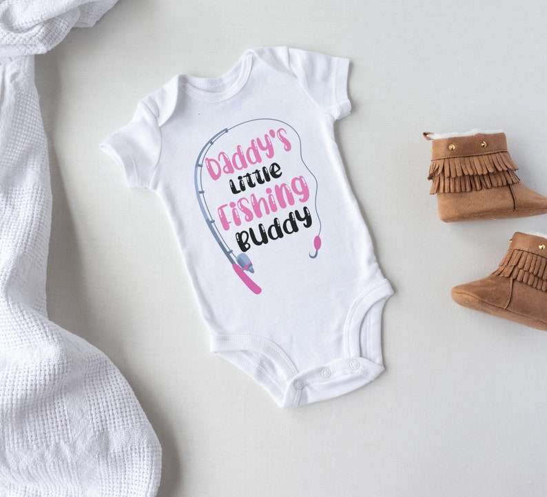 May include: White baby onesie with a pink fishing rod and the text "Daddy's little fishing buddy".