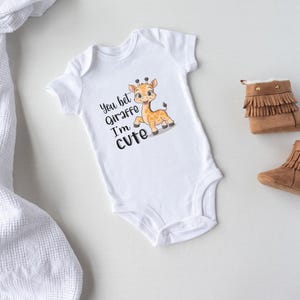 May include: White baby onesie with a cute cartoon giraffe and the text "You bet Giraffe I'm cute".
