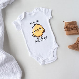 May include: White baby onesie with a yellow chick cartoon and the text "New to the coop".