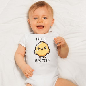 May include: A white baby onesie with a yellow chick cartoon and the text "New to the coop".