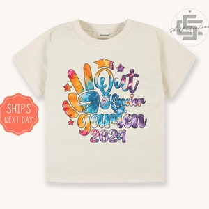 May include: A white t-shirt with a tie-dye design featuring the text "I'm Outta Kindergarden 2024" in colorful letters with a peace sign and stars.