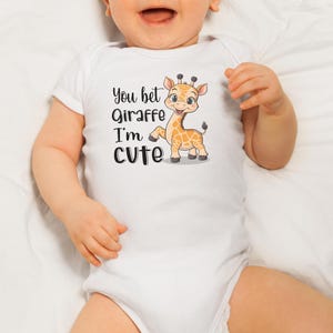 May include: White baby onesie with short sleeves featuring a cartoon giraffe with the text "You bet giraffe I'm cute".