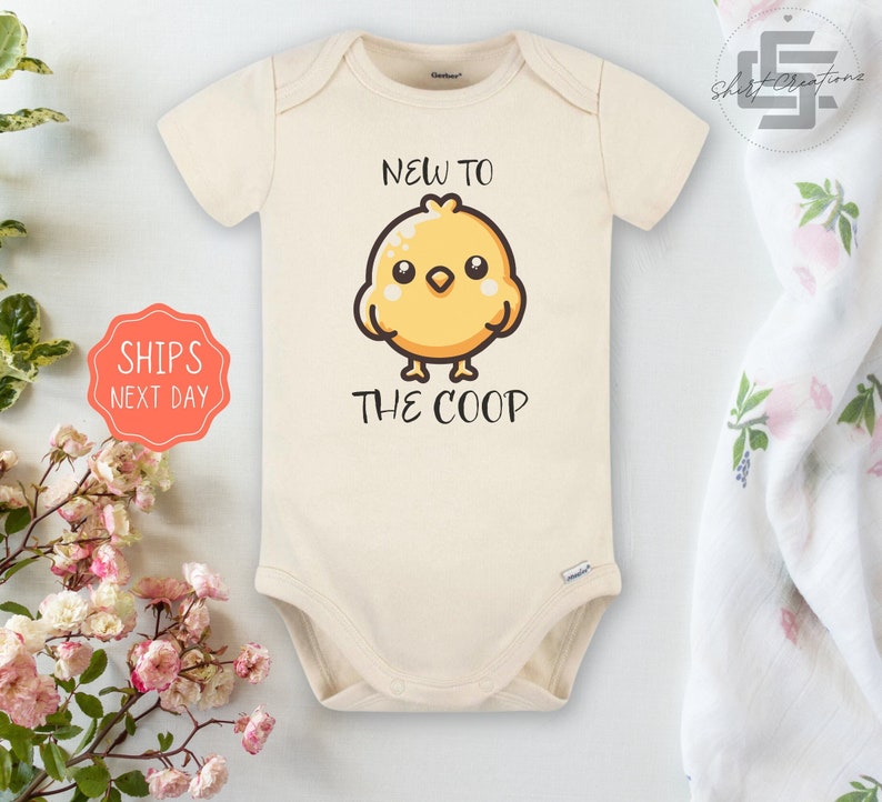 May include: A cream-colored baby onesie with a cute cartoon chick and the text "New to the Coop".