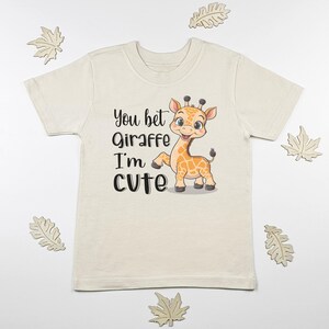 May include: A cream colored t-shirt with a cartoon giraffe and the text "You bet Giraffe I'm cute".