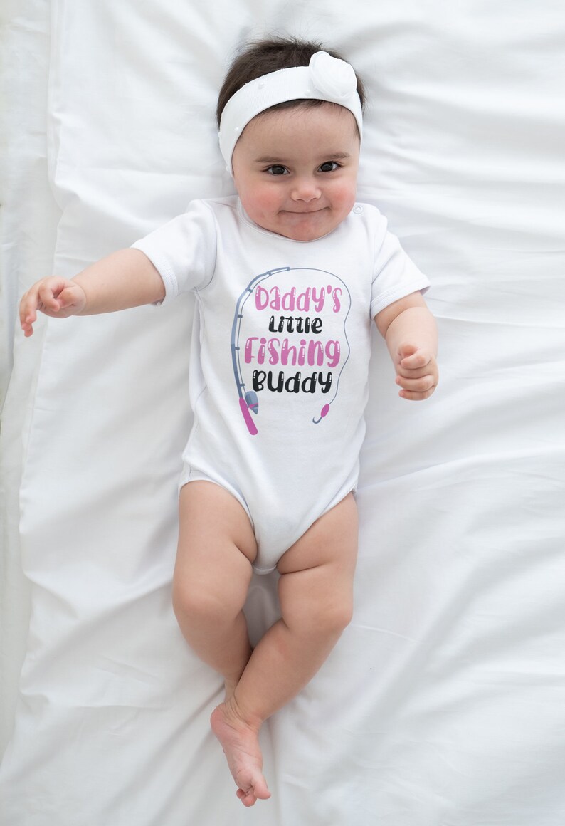 May include: White baby onesie with a pink and gray graphic that says "Daddy's little Fishing Buddy" with a fishing rod and hook.
