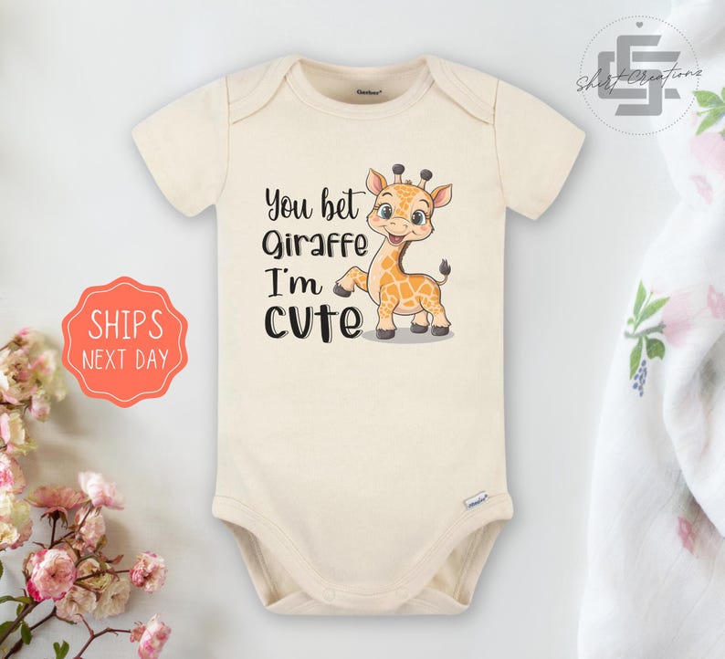 May include: A cream colored baby onesie with a cartoon giraffe and the text "You bet Giraffe I'm cute".
