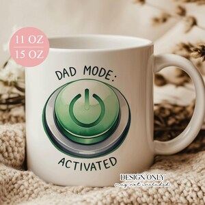 May include: White ceramic mug with the text "DAD MODE: ACTIVATED" and a green power button graphic. The mug has a capacity of 11 oz or 15 oz. The design is printed on the front of the mug.
