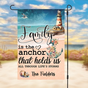 May include: A garden flag with a beach scene, a lighthouse, an anchor with flowers, and the text "Family is the anchor that holds us all through life's storms". The flag also has the text "The Fielders" at the bottom.