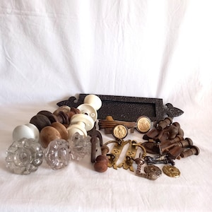 May include: A selection of antique door furniture, featuring glass, wooden, and metal knobs, pulls, and a decorative letter plate. The hardware components are in diverse forms and dimensions, with colours from clear to dark brown.