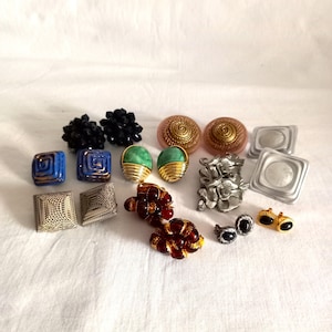 Könnte beinhalten: Eine Sammlung von Vintage-Ohrringen in verschiedenen Stilen und Farben. Enthält schwarze Perlen, blaue und goldene Quadrate, grüne und goldene, rosa Wirbel, silberne Blumen und andere einzigartige Designs. Eine Vielzahl von Clip-On- und Stecker-Ohrringen wird gezeigt.