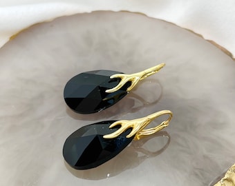 May include: A pair of black teardrop-shaped earrings with gold antlers. The earrings are on a white surface.