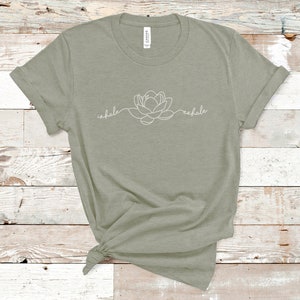 May include: A sage green t-shirt with a white outline of a flower and the words "inhale" and "exhale" on the front.