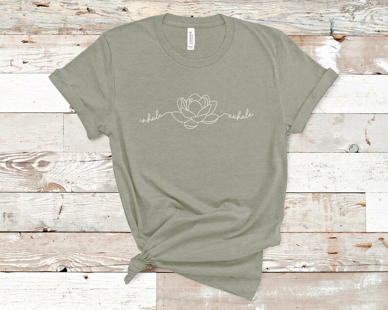 May include: A sage green t-shirt with a white outline of a flower and the words "inhale" and "exhale" on the front.